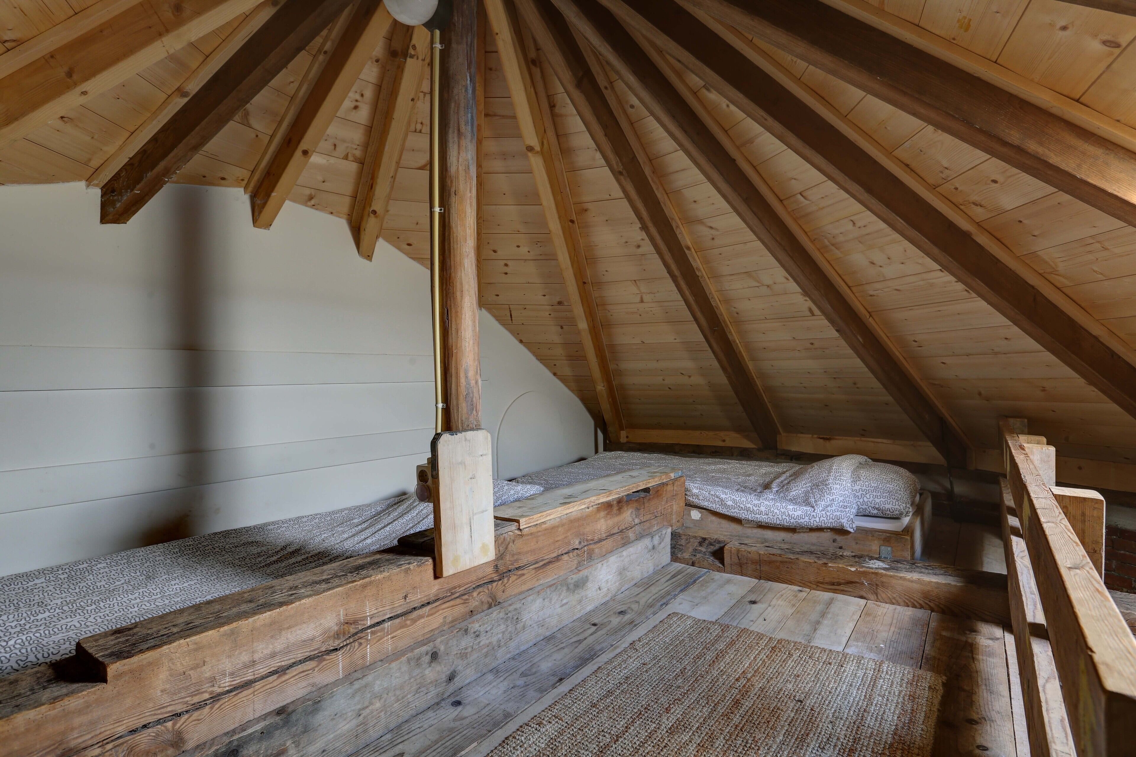 A loft bedroom with wooden beams, a sloped ceiling, and a simple bed setup.