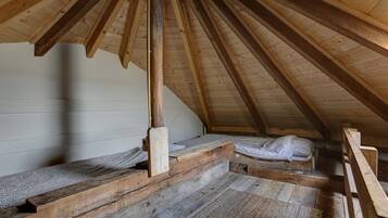 A loft bedroom with wooden beams, a sloped ceiling, and a simple bed setup.