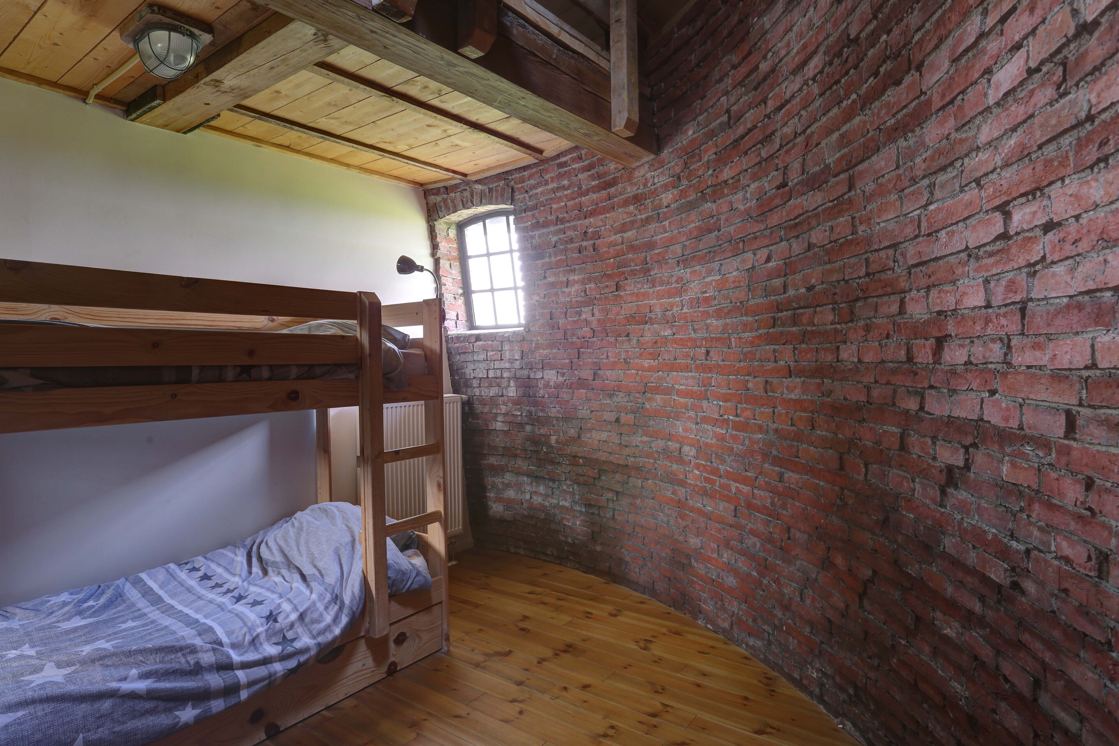A room with a bunk bed, a window, and a brick wall.