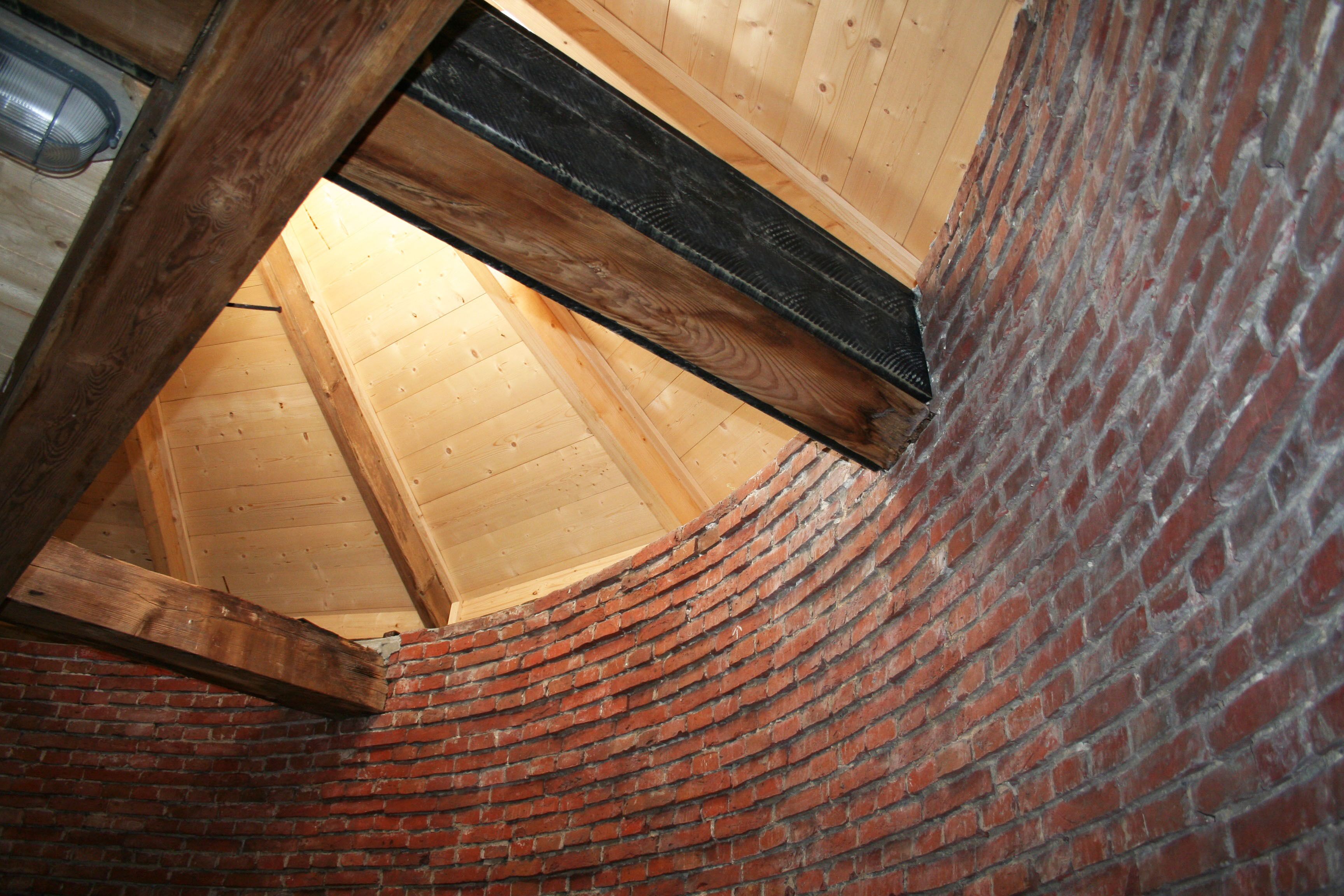 Un muro de ladrillo curvo con estructura de viga de madera y techo inclinado.