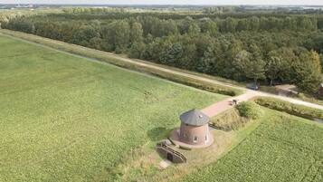 Een landelijk landschap met een rond gebouw in de buurt van een weg, omgeven door velden en bomen.