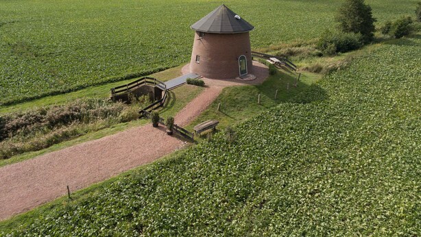 Ein rundes Backsteingebäude mit einem Kegeldach, umgeben von einem Kiesweg und Holzzaun.