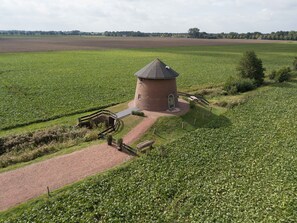 Un bâtiment circulaire en briques, surmonté d’un toit conique, entouré d’un chemin de gravier et de clôtures en bois.