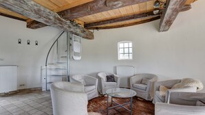 Ein geräumiges Wohnzimmer mit weißen Ledersofas, einem Glastisch und einer rustikalen Holzbalkendecke.