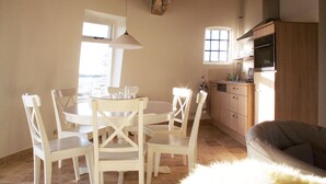 Ein Essbereich mit einem runden Tisch und weißen Stühlen, eine Küche mit Holzschränken und ein graues Sofa.