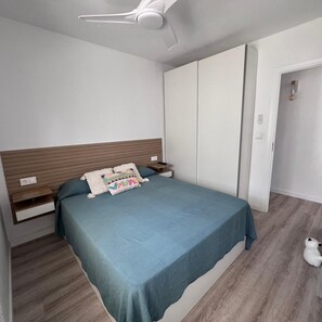 A bedroom with a bed, bedside tables, a wardrobe, a ceiling fan, and a small white dog. - 172 Holiday Beach (Denia)