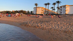 Een strand met palmbomen, mensen die ontspannen, en gebouwen op de achtergrond.