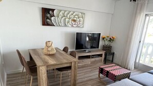 Een moderne woonkamer met een houten eettafel, een grijze bank en een flatscreen televisie.