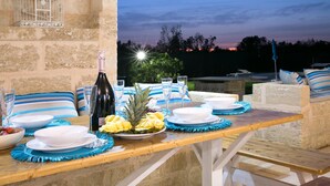A table set for a meal with plates, glasses, and a bottle, surrounded by stone walls and a view of the sky.
