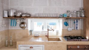 A kitchen with a wooden shelf holding kitchenware, a gas stove, and a sink with a faucet.