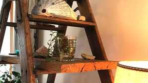 Eine rustikale Holzleiterregal mit verschiedenen Gegenständen, darunter ein Ventilator, ein Glas mit Wasser und eine Pflanze, sowie dekorative Objekte.