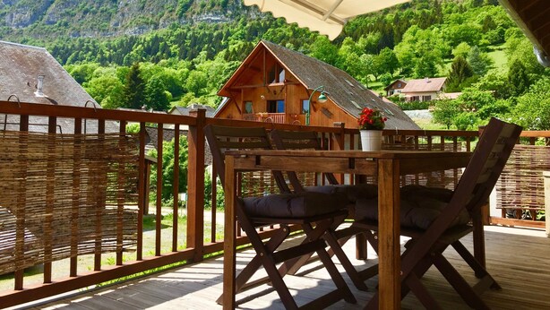 Eine Holzterrasse mit Tisch und Stühlen mit Blick auf eine gebirgige Landschaft.