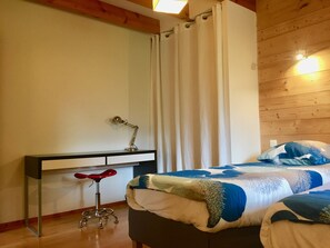 A bedroom with a bed, a desk with a chair, a lamp, and a curtain.