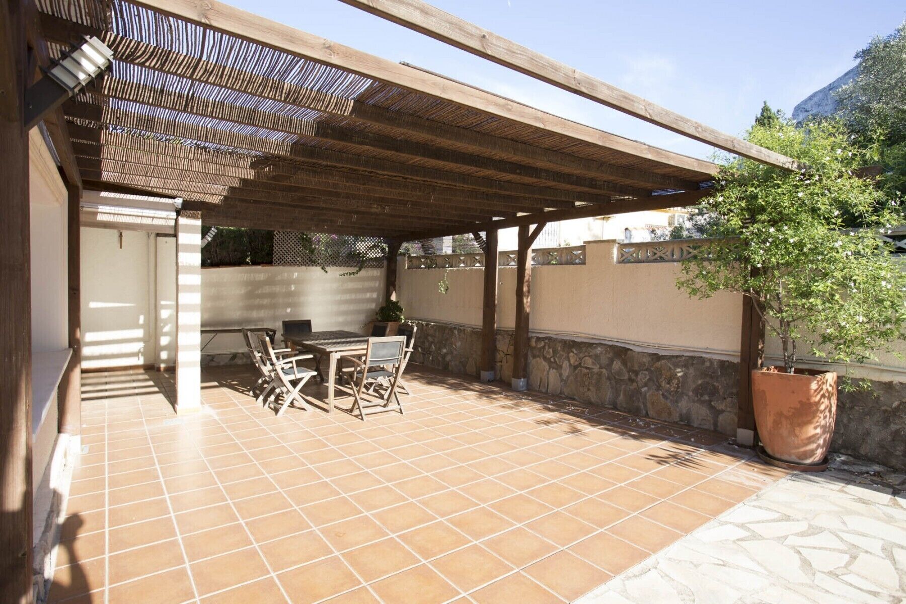 A covered patio with a tiled floor, a table with chairs, and a potted plant.