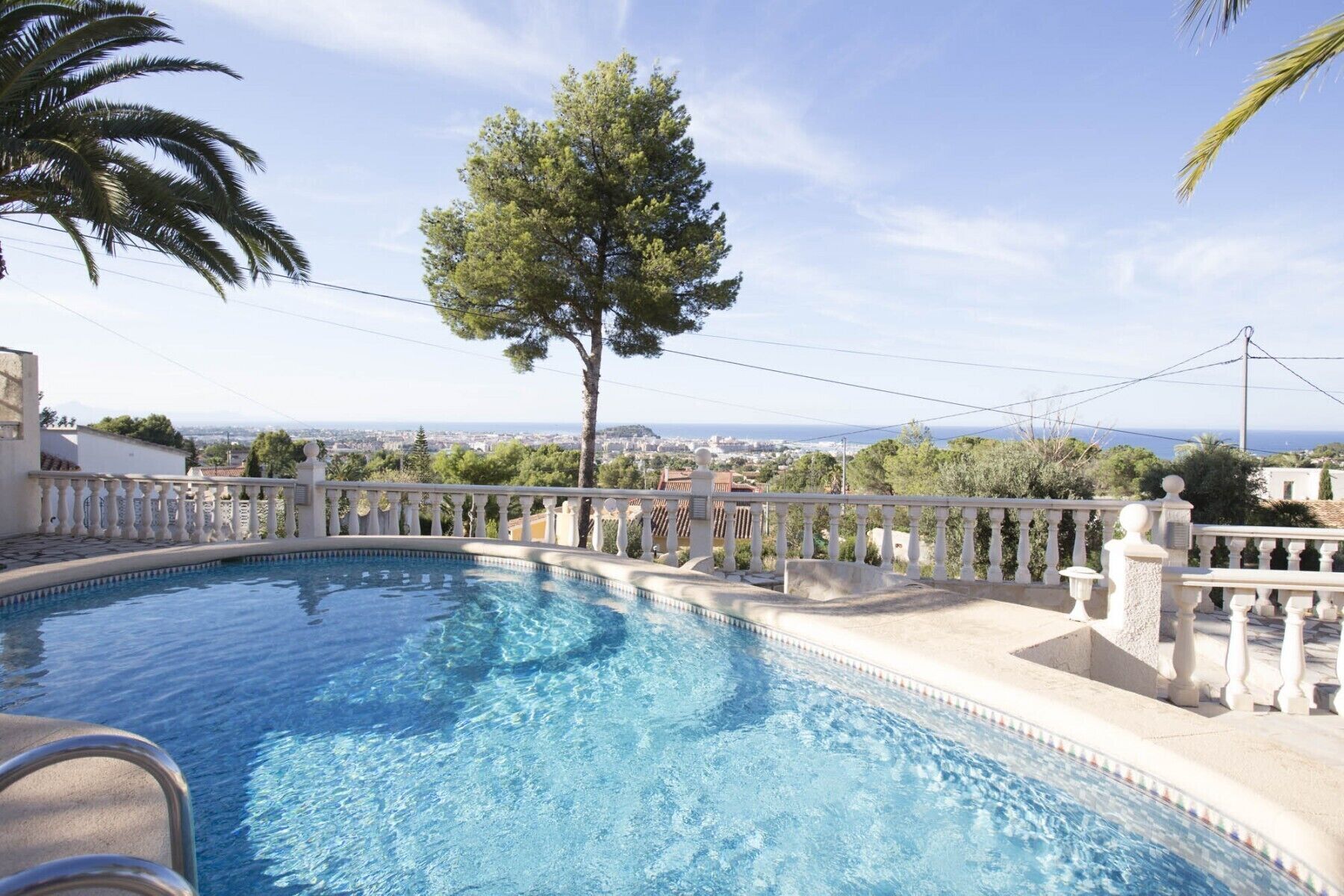 A swimming pool with a white balustrade, a tree, and a view of a cityscape.