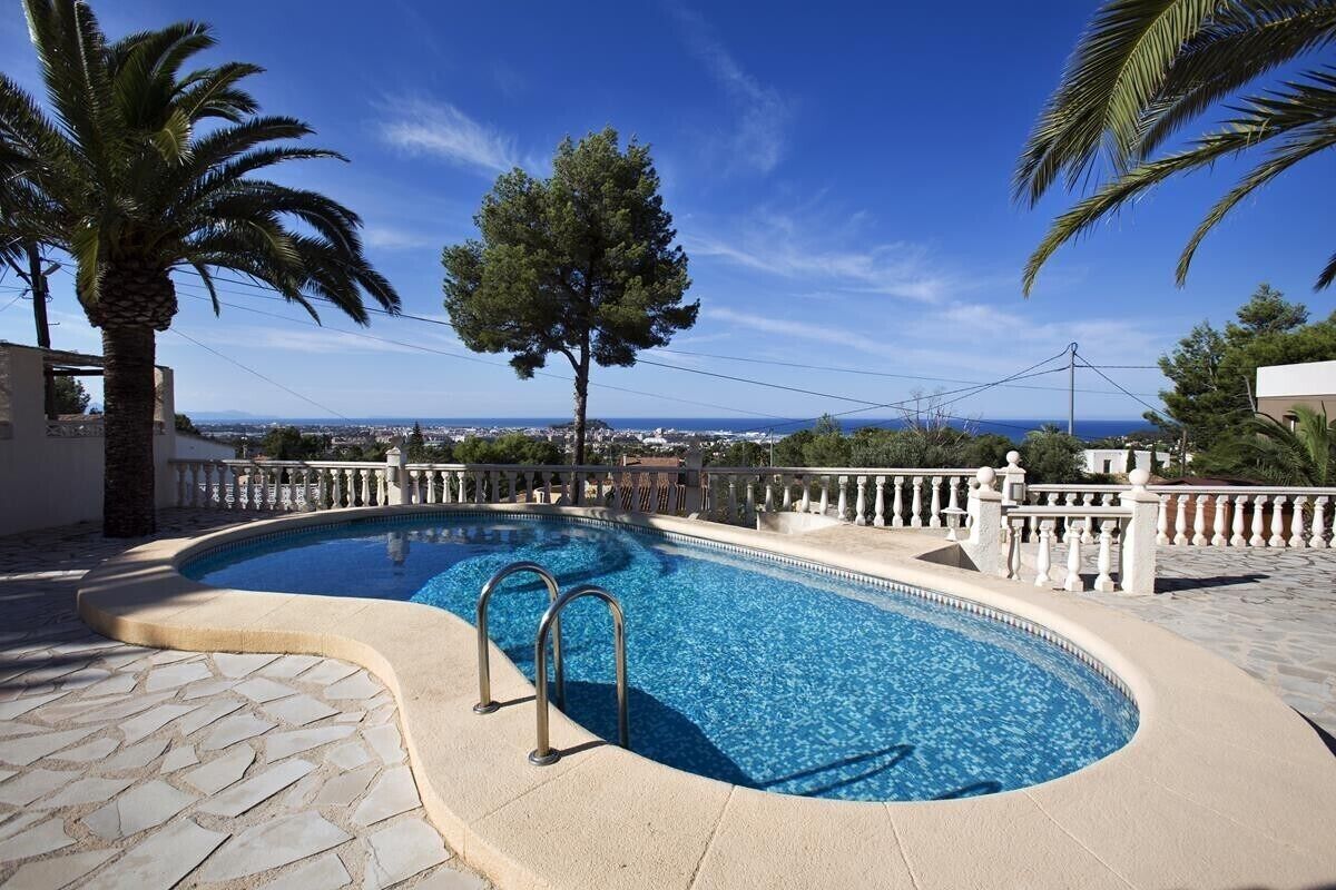 A swimming pool with a curved edge, surrounded by stone tiles and a white fence.