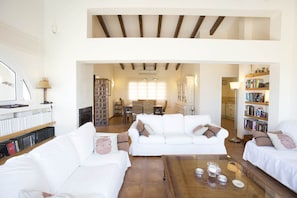A spacious living room with white sofas, a coffee table, and a bookshelf.