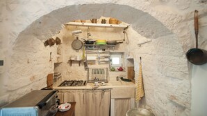 A compact kitchen with a rustic stone wall, a small window, and basic appliances. - Il Trullo di Ben (Locorotondo)