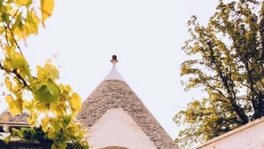 A small stone building with a conical roof, an arched entrance, and a patio area with chairs and potted plants. - Il Trullo di Ben (Locorotondo)