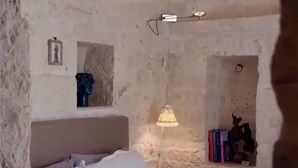 A room with a bed, a lamp, a shelf with books, and a wall-mounted light fixture. - Il Trullo di Ben (Locorotondo)