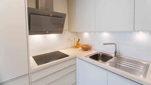 Une cuisine moderne avec des meubles blancs, un évier en acier inoxydable et une cuisinière intégrée.
