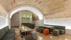 Un salón moderno con techo de ladrillo, sofás verdes, una mesa larga y una zona de bar con botellas.