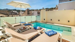 Zona de piscina en la azotea con sillones y una sombrilla.