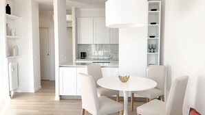 A modern, minimalist living room with a round white table, four white chairs, and a large white pendant light.