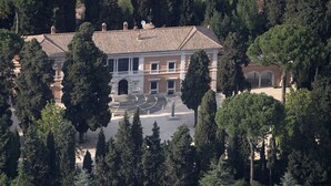A large, historic building with a symmetrical facade, central courtyard, and surrounding mature trees.