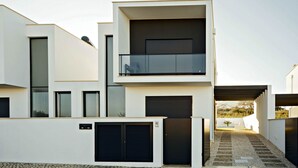 Un bâtiment moderne à deux étages, doté d’un balcon, de grandes fenêtres et d’un espace d’entrée pavé.
