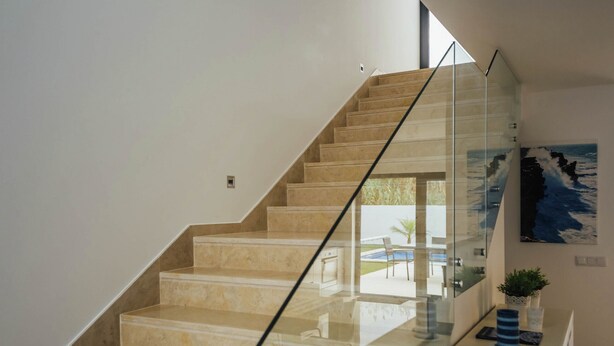 Un escalier avec des rampes en verre menant à un espace extérieur doté d’une piscine et de chaises.