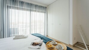 Un lit bien fait, avec un oreiller bleu, un plateau contenant des articles pour le petit-déjeuner et un magazine posé sur le lit.