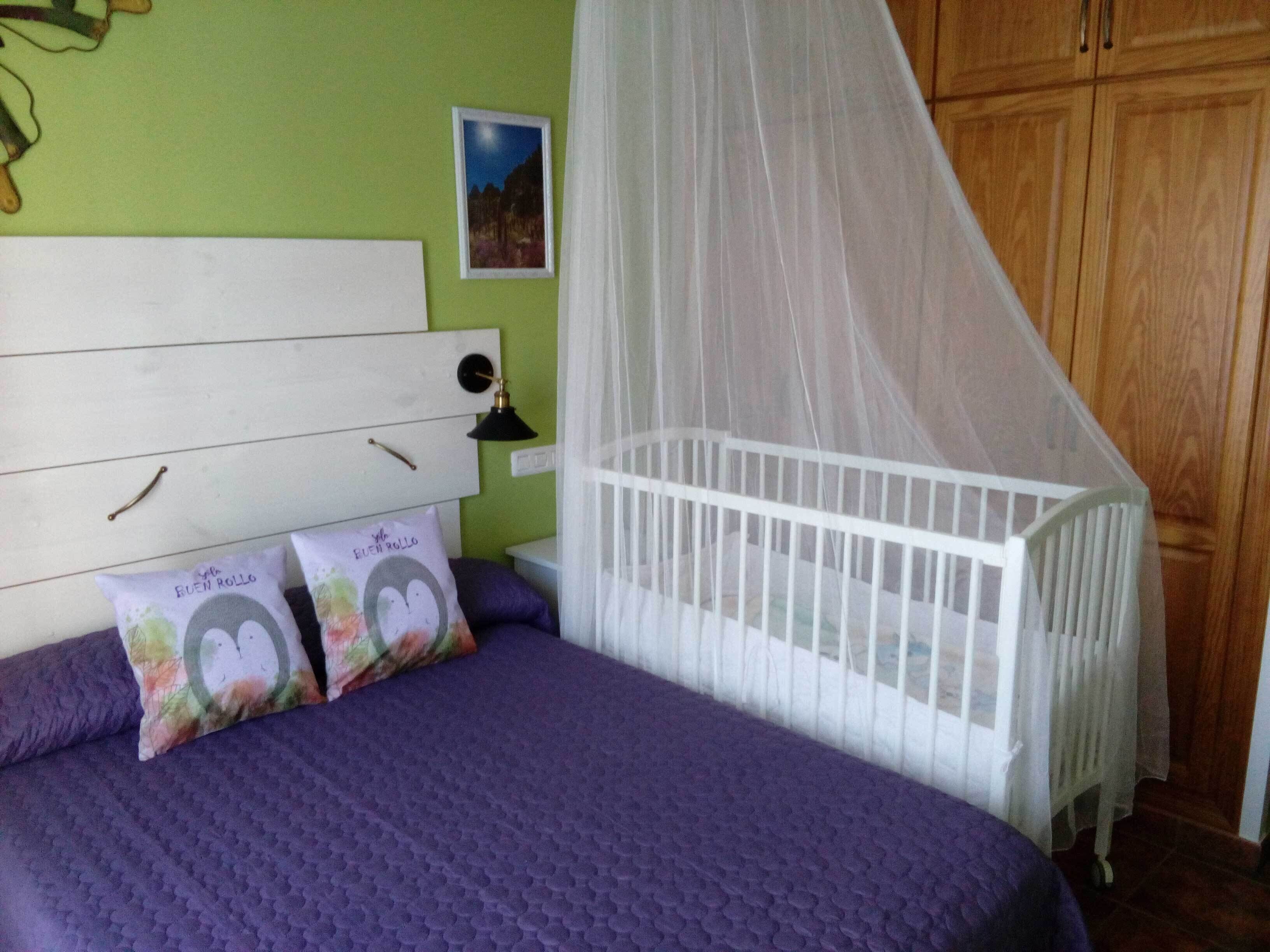 A bedroom with a bed, a crib, a nightstand, and a green wall.