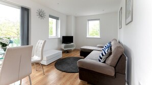 A modern living room with a sofa, a white chair, a TV, and a small table. - Skyvillion - 1Bed Enfield Flat w/Balcony+Parking (Greater London)