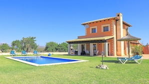 Una casa de dos pisos con piscina, mobiliario exterior y zona de patio.
