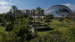 A modern building with a unique curved roof, surrounded by a well-maintained park with palm trees and pathways. - Singular Stays Botanico Room IV (Valencia ciudad)