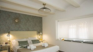 A modern hotel room with a large bed, bedside lamps, a window with curtains, and a small table with a cup and a bowl of fruit. - Singular Stays Botanico Room IV (Valencia ciudad)
