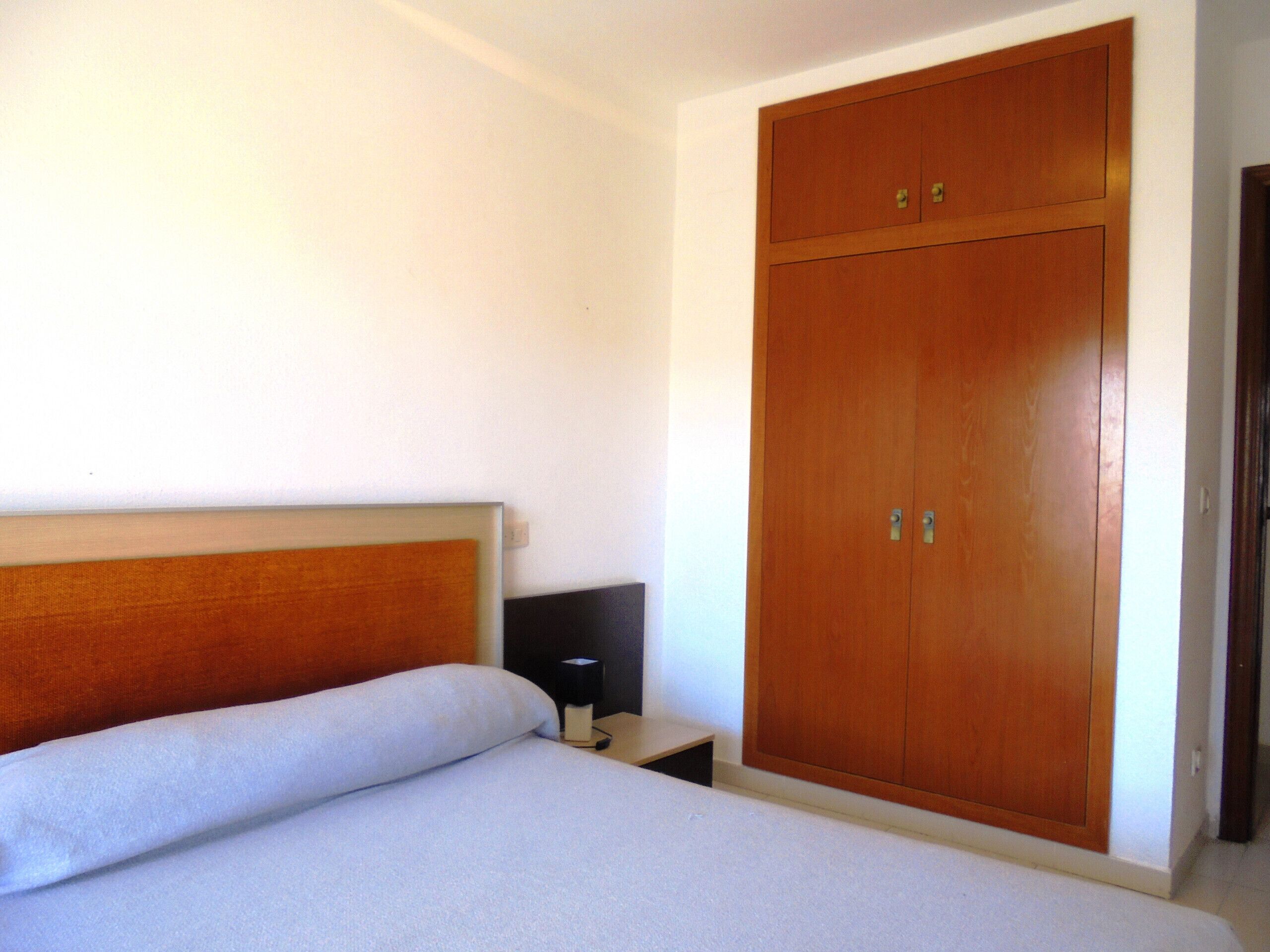 Un dormitorio con cama, mesita de noche y armario de madera.