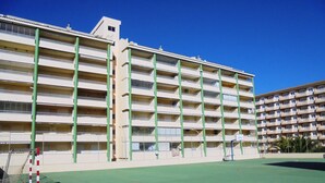 Een hotel met meerdere verdiepingen, balkons, een basketbalveld en een helderblauwe lucht.