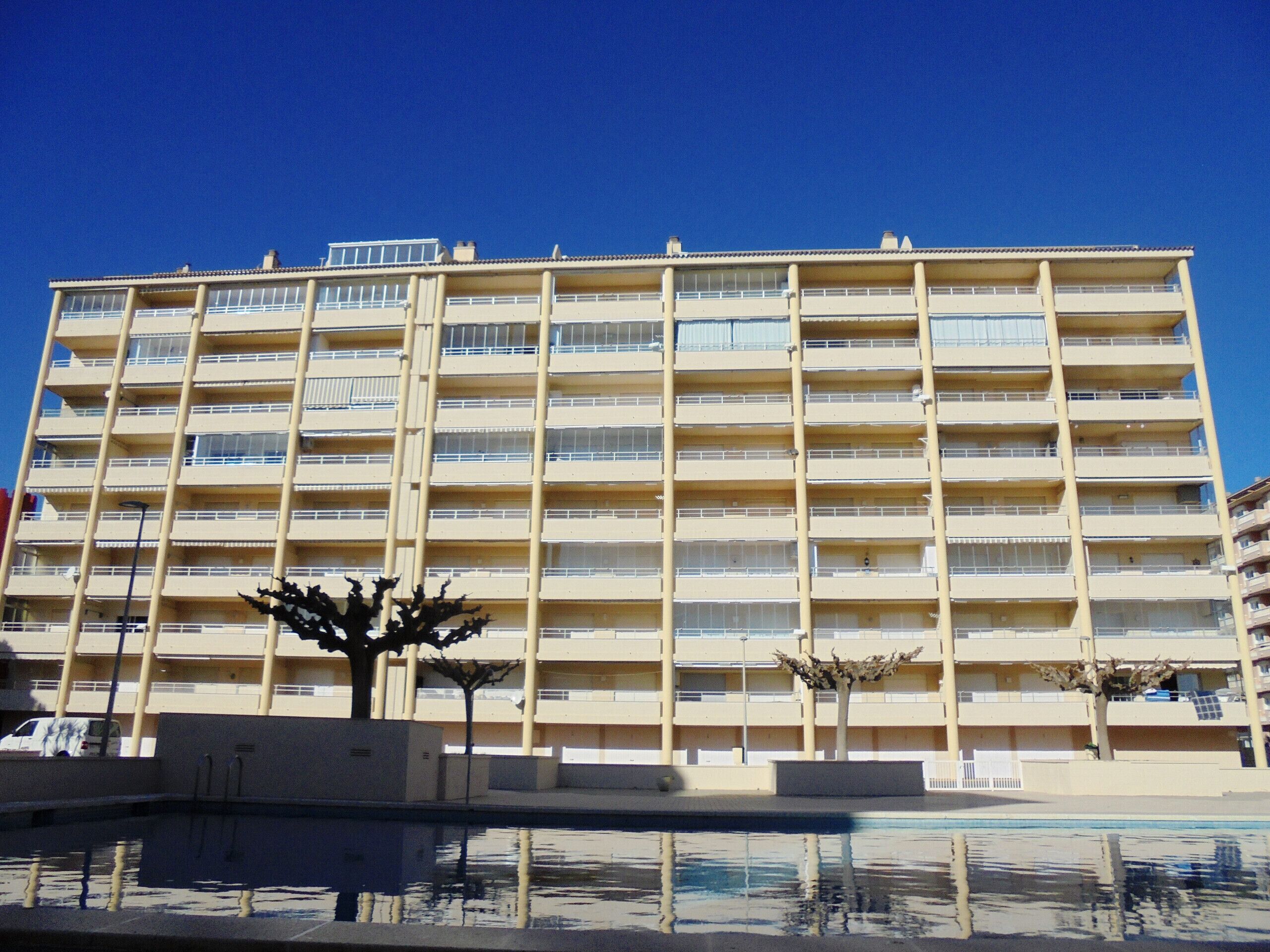 Un immeuble à étages doté d’une façade uniforme, de balcons et d’un bassin d’eau réfléchissant en premier plan.