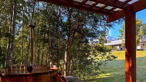 Un bain à remous installé sous une pergola en bois, avec vue sur une zone herbeuse et des arbres.