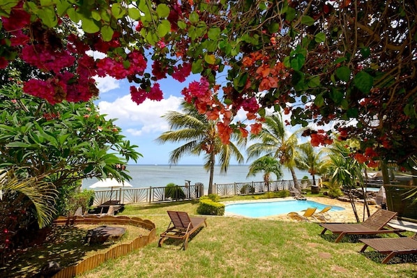 A pool area with lounge chairs, a wooden deck, and a view of the ocean.