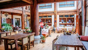 A spacious interior with wooden furniture, a central seating area, and a large bookshelf filled with books. - Shangri-La E-Outfitting Boutique Hotel (Deqin)