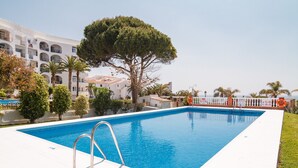 Una piscina con cubierta blanca, rodeada de palmeras y un edificio con balcones.