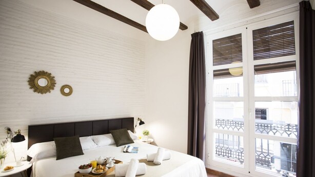 Een hotelkamer met een groot bed, een ronde lamp, een balkon met een hekwerk en een raam met jaloezieën.