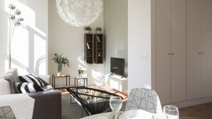 Een moderne woonkamer met een bank, eettafel en stoelen, een hanglamp en een televisie op een dressoir.
