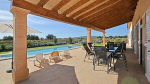 Ein überdachter Außenbereich mit Pool, Liegestühlen und einem Tisch.