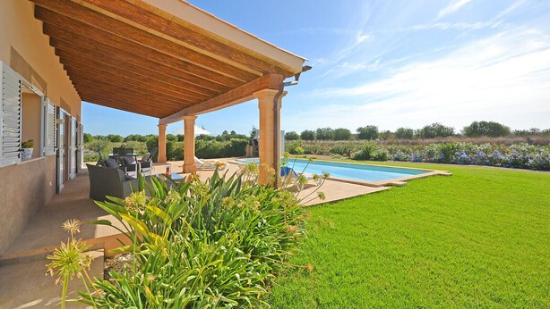 Ein überdachter Patio-Bereich mit Gartenmöbeln, einem Schwimmbad und einem gepflegten Rasen.