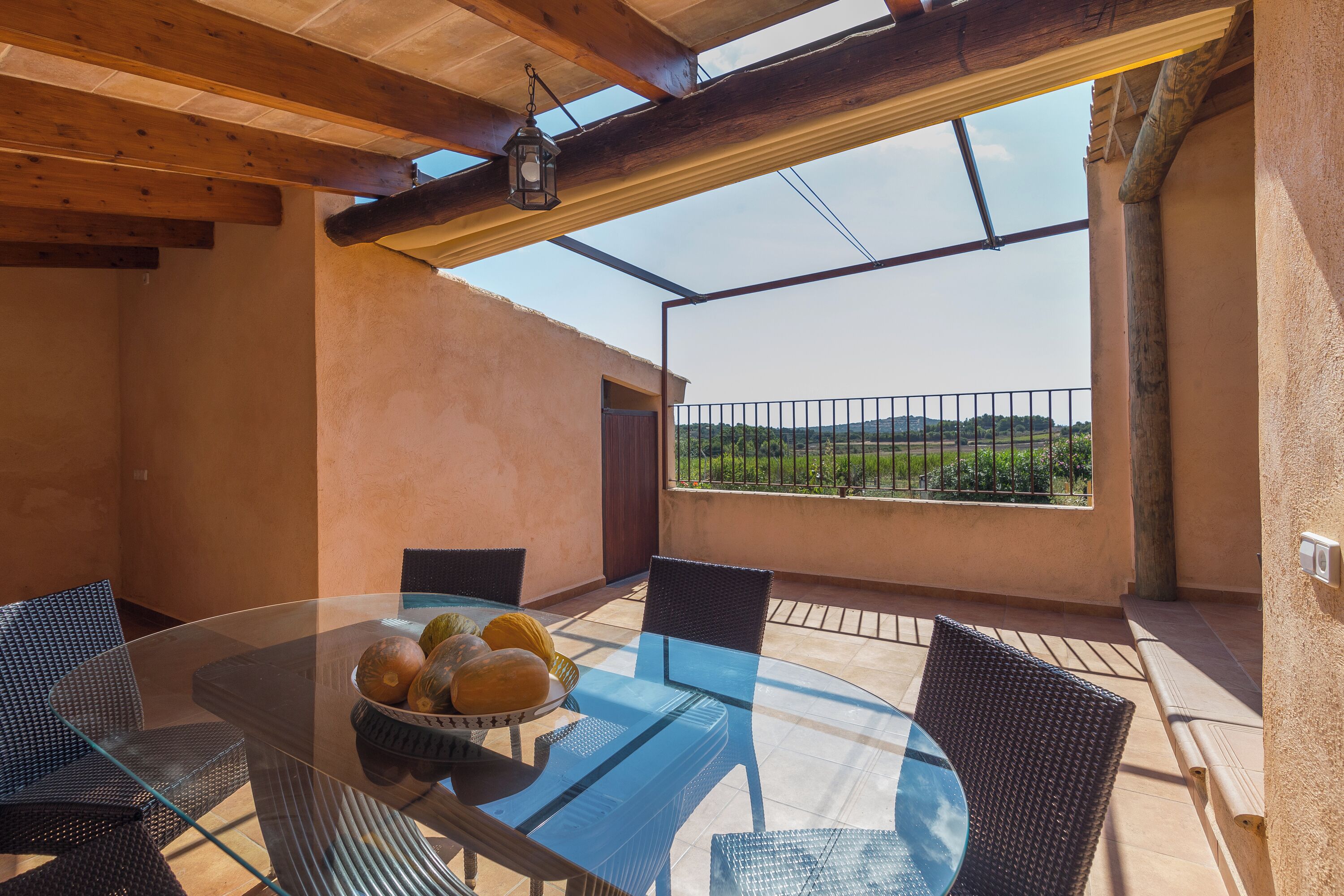 Une terrasse extérieure avec une table en verre, des chaises en osier et une vue sur la campagne.