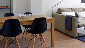 A modern living room with a wooden dining table, black chairs, a beige sofa, and a floor lamp.